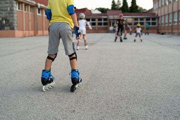 Back view of young boy riding roller blades skates and safety equipment in the school yard in summer day