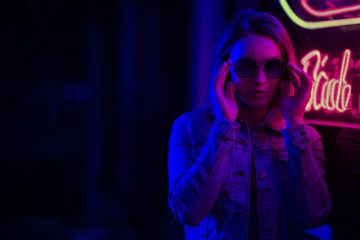 Fototapeta na wymiar Sexy portrait of a young girl with an open bust in sunglasses and with in the night city, red-blue light of neon lamps. Night clubs, parties, strip business, night life, business game. Banner