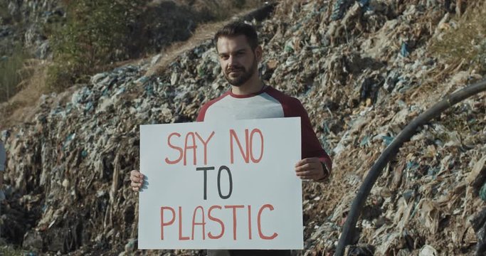 Eco volunteer showing text of Say no to Plastic inspiring poster while staying at disposal site out of town. Environmental concerns.