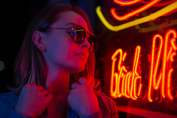 Street fashion young girl with sunglasses, neon light red blue, nightlife and trendy lifestyle
