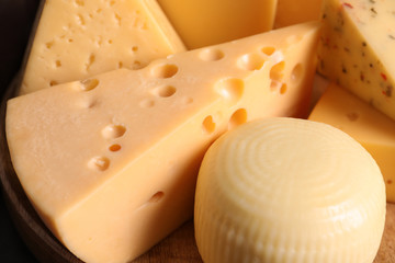 Different kinds of tasty cheese on wooden plate, closeup