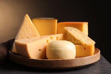 Wooden plate with different sorts of cheese on grey table