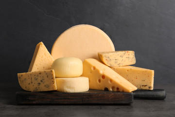 Wooden board with different sorts of cheese on grey table