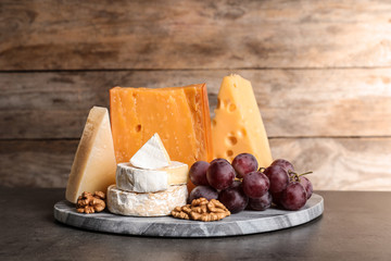 Composition with assorted cheese, grapes and walnuts on table against wooden background