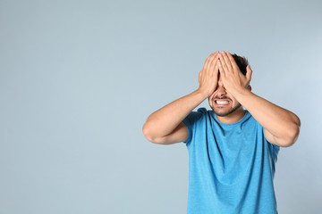 Young man being blinded on grey background, space for text