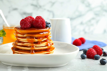 Delicious pancakes with fresh berries and syrup on grey table