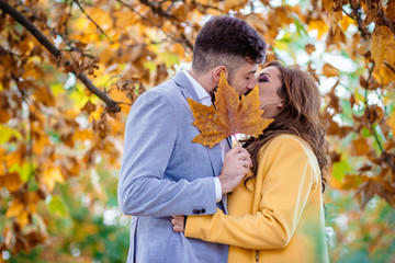 Fototapeta premium Outdoors photo, beautiful, young couple kissing behind the yellow oak leaf.