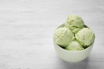 Tasty pistachio ice cream on white wooden table, space for text