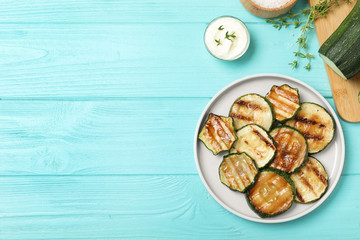 Plate of delicious grilled zucchini slices on light blue wooden table, flat lay. Space for text