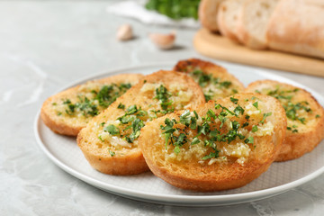 Slices of toasted bread with garlic and herb on light grey marble table, closeup