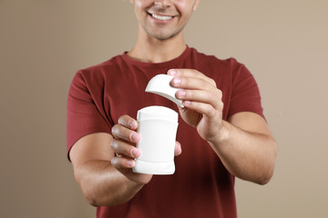 Young man holding deodorant on beige background, closeup. Mockup for design