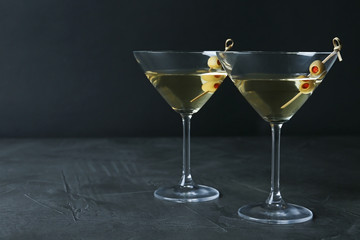 Glasses of Classic Dry Martini with olives on dark table against black background. Space for text