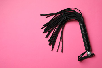 Black whip on pink background, top view with space for text. Sexual role play accessory