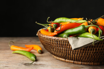Wicker bowl with different chili peppers on wooden table, closeup. Space for text