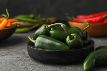 Black wooden bowl with green hot chili peppers on grey table