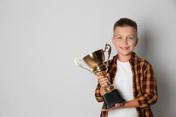 Happy boy with golden winning cup on light background. Space for text © New Africa