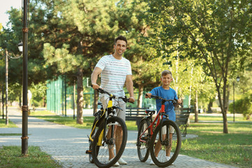 Obraz premium Dad and son riding bicycles in park on sunny day