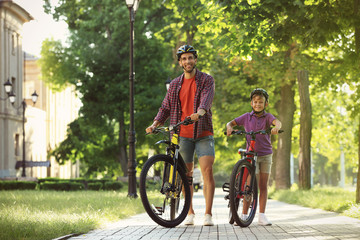 Dad and son riding bicycles in park on sunny day