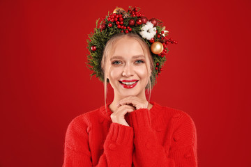 Beautiful young woman wearing Christmas wreath on red background