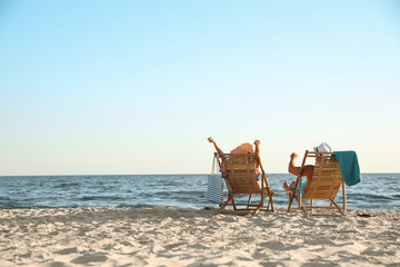 Fototapeta na wymiar Young couple relaxing in deck chairs on beach near sea