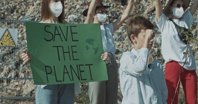 Cute smiling boy protesting with ecology volunteers on strike staying at waste dump. Environmental movement. Fighting pollution.
