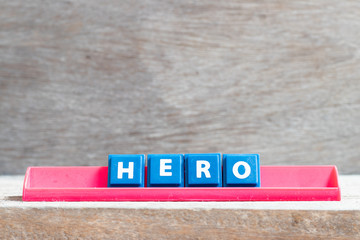 Tile letter on red rack in word hero on wood background