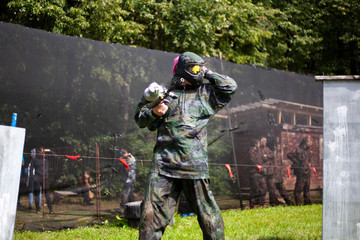 Injured paintball player. The equipped warrior leaves the battlefield. A guy in a mask and with a gun for shooting with paint.