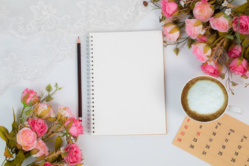 Top view flat lay wedding concept with notebook mock up for checklist and pencil decorated with lace, beautiful pink rose bouquet flowers, calendar and coffee cup with copy space on white background