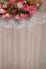 Selective focus top view of flat lay of beautiful pink rose bouquet on white elegant lace on wooden background with copy space, greeting season, anniversary or wedding concept