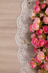 Selective focus top view of flat lay of beautiful pink rose bouquet on white elegant lace on wooden background with copy space, greeting season, anniversary or wedding concept