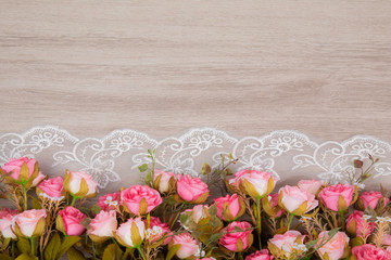 Selective focus top view of flat lay of beautiful pink rose bouquet on white elegant lace on wooden background with copy space, greeting season, anniversary or wedding concept