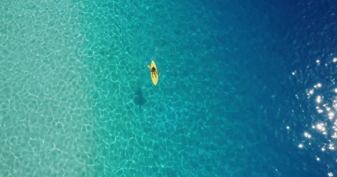 Aerial view of a woman in a yellow kayak paddling in pristine sunny blue ocean lagoon water