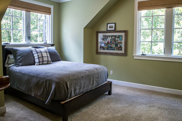 A bedroom with green walls and gray bedding and a plaid pillow with a window behind the bed