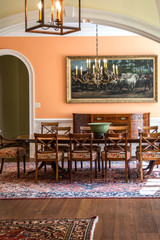 Orange peach colorful dining room with oriental rug and classic wood chairs and table with chandelier and artwork.