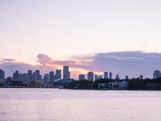 Miami city skyline panorama at dusk with urban skyscrapers and bridge over sea with reflection