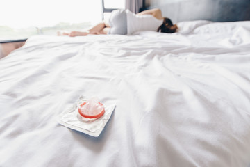 Shot of woman sleeping on bed with a small condom after tearing placed on the bed. Safe sex and Prevent Pregnancy concept.