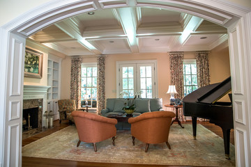 large formal living room in a spacious home. Arched doorway entrance and comfortable furniture with a baby grand piano. Coffered ceiling and a lot of natural light from the large windows.