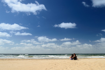 Horizonte de mar con mujeres abrazadas en la playa en día soleado con cielo azul y nubes