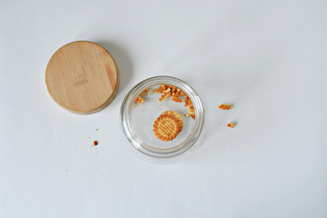 Glass jar with wooden cover and cookie leftovers over white