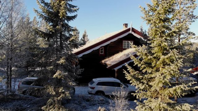 Dolly movement with snow covered trees in foreground and wooden cabin in background with cars