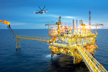 Offshore oil and gas rig platform with offshore helicopter transporting to oil rig at beautiful sky...