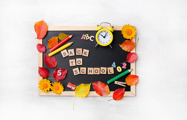 back to school concept. cute stationery - pencil, clock alarm, autumn leaves on black chalkboard. Concept of education, starting school, beginning of school year. flat lay, copy space