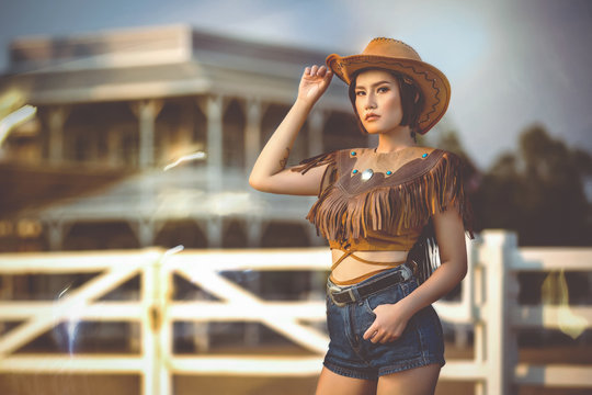 Asian girl in a cowgirl outfit standing at the farm fence.