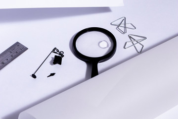 Lupa sobre escritorio blanco y rollos de papel preparados para dibujar en ellos. Con miniaturas de...