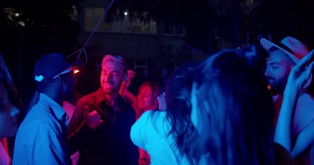 At night crowd or group of young multi-ethnic people during dancing colorful party in different clothes drinking alcohol having fun on weekend laughing sharing celebration close up slow motion