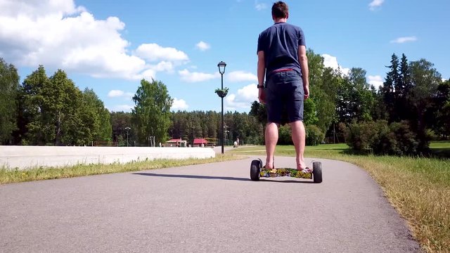 A man drives his hover board away along the path and nearly falls. A long steady shot