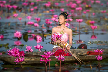 Asia women on the boat in the lotus pond. She wears Thai traditional dresses.