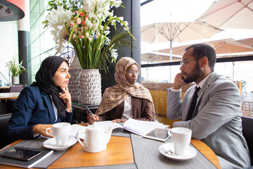 Multiethnic business partners working on agreement in cafe. Businessman and Muslim businesswomen...