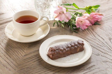 Chocolate cake with caramel, peanuts and almonds and cup of black tea and flowers on wooden table