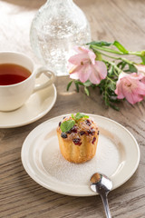 Fototapeta na wymiar Cranberry muffin with mint leaf and cup of black tea and flowers on wooden table